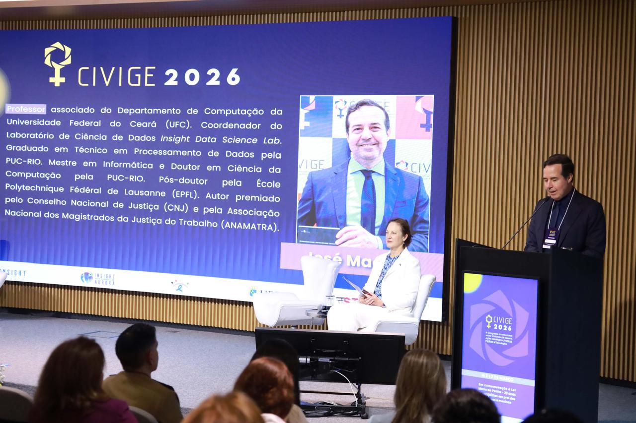 Uma fotografia do palco de uma conferência com Sophie Davies, Embaixadora da Austrália, sentada em uma poltrona branca, e José Macêdo, coordenador do Insight Lab, de pé atrás de um púlpito. Uma grande tela de LED ao fundo exibe o logotipo "CIVIGE 2026" e um texto biográfico sobre Macêdo. Davies está à esquerda e Macêdo à direita, com uma plateia visível em primeiro plano.