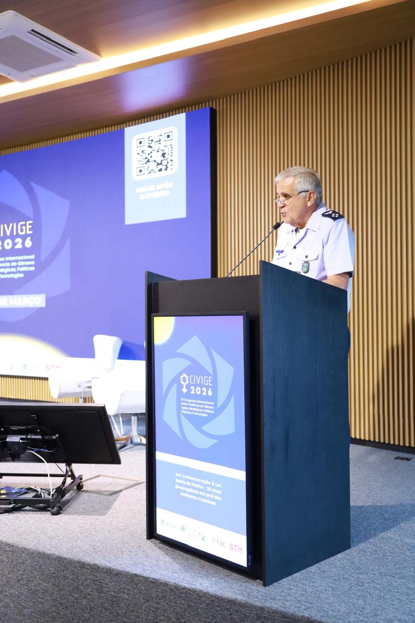 Ministro Tenente-Brigadeiro do Ar Francisco Joseli Parente Camelo fala em um púlpito preto durante o CIVIGE 2026. O monitor do púlpito e o grande painel de LED ao fundo exibem o logotipo do evento e informações sobre o congresso, incluindo um código QR.