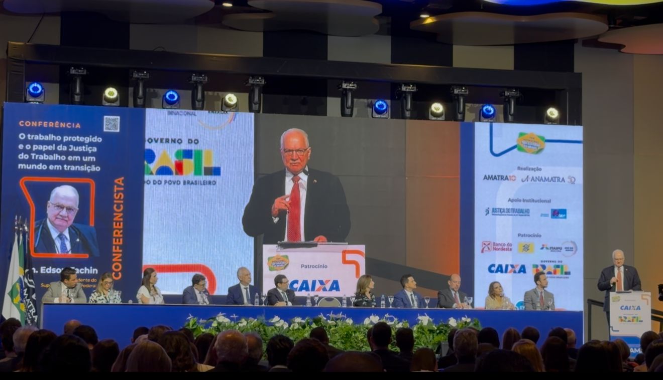 Ministro Edson Fachin discursa no 22º Conamat, em auditório com plateia, enquanto sua imagem é exibida em telão ao fundo e autoridades compõem a mesa no palco.